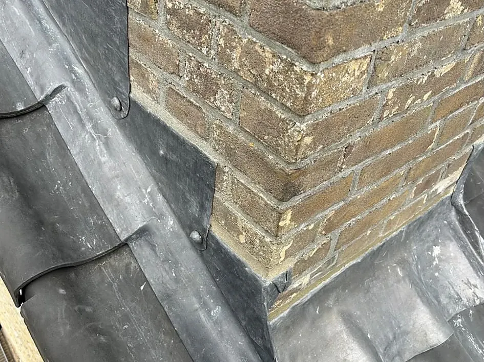 Nieuw loodwerk rond een gemetselde schoorsteen op een pannendak